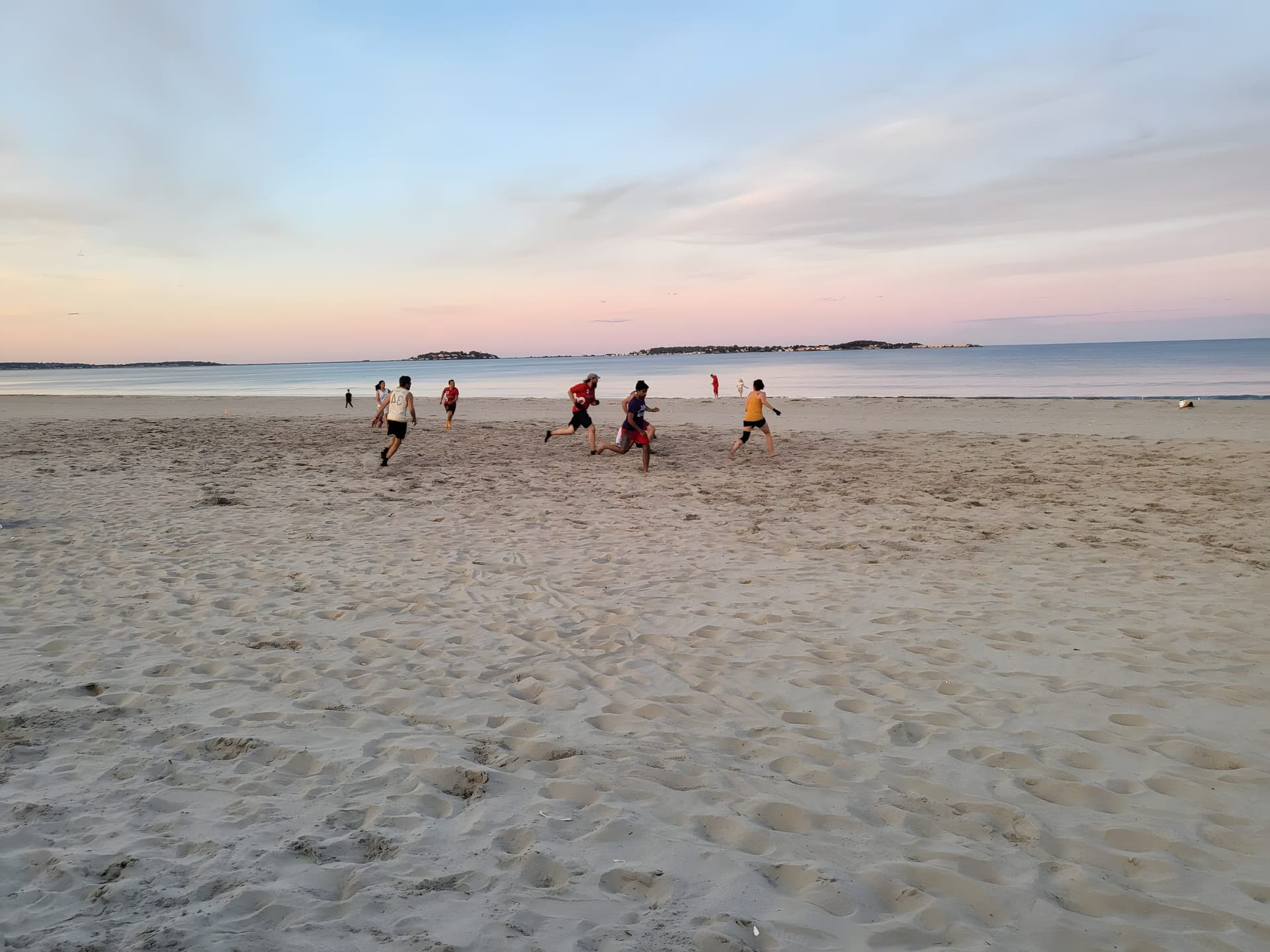 Beach league at Revere at dusk — players sprinting on sand under a pastel sunset