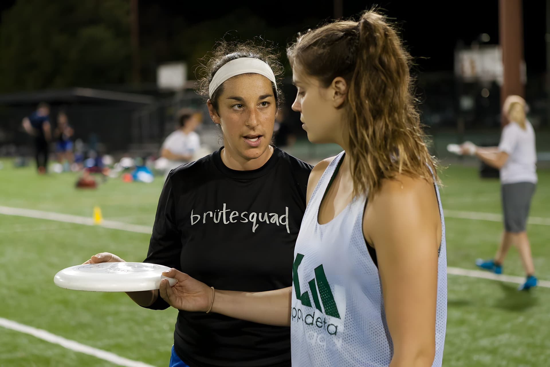 Coach with a disc instructing a player under stadium lights at night practice