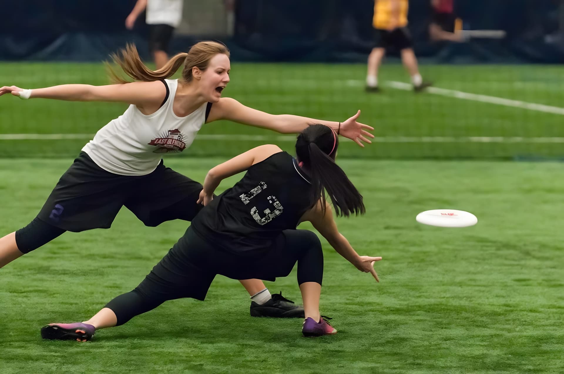 Indoor turf league — two players lunging on defense as the disc flies past