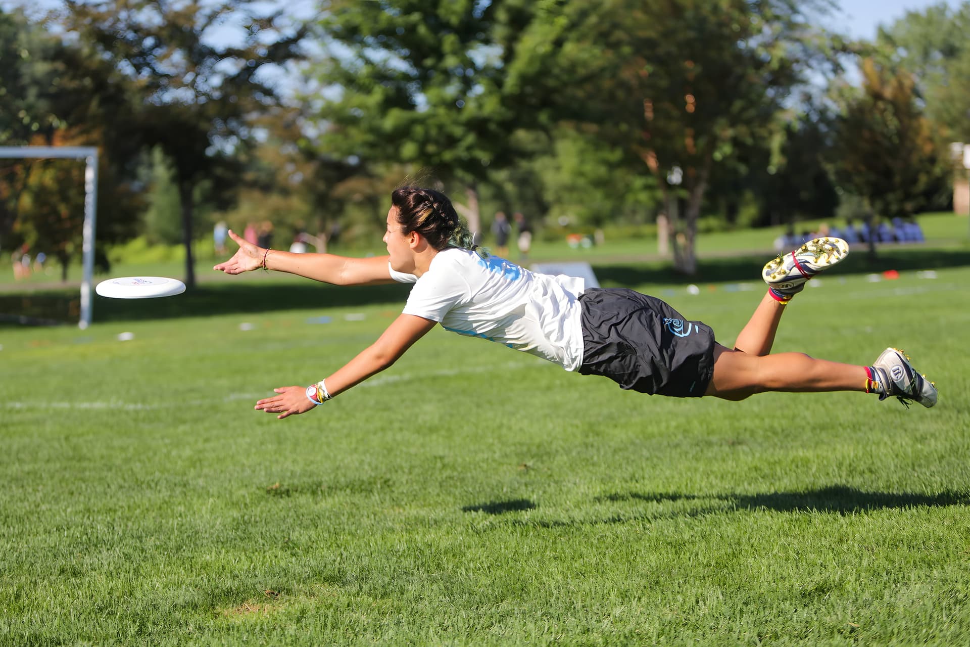 A BUDA player fully laid out, parallel to the grass, reaching for a disc