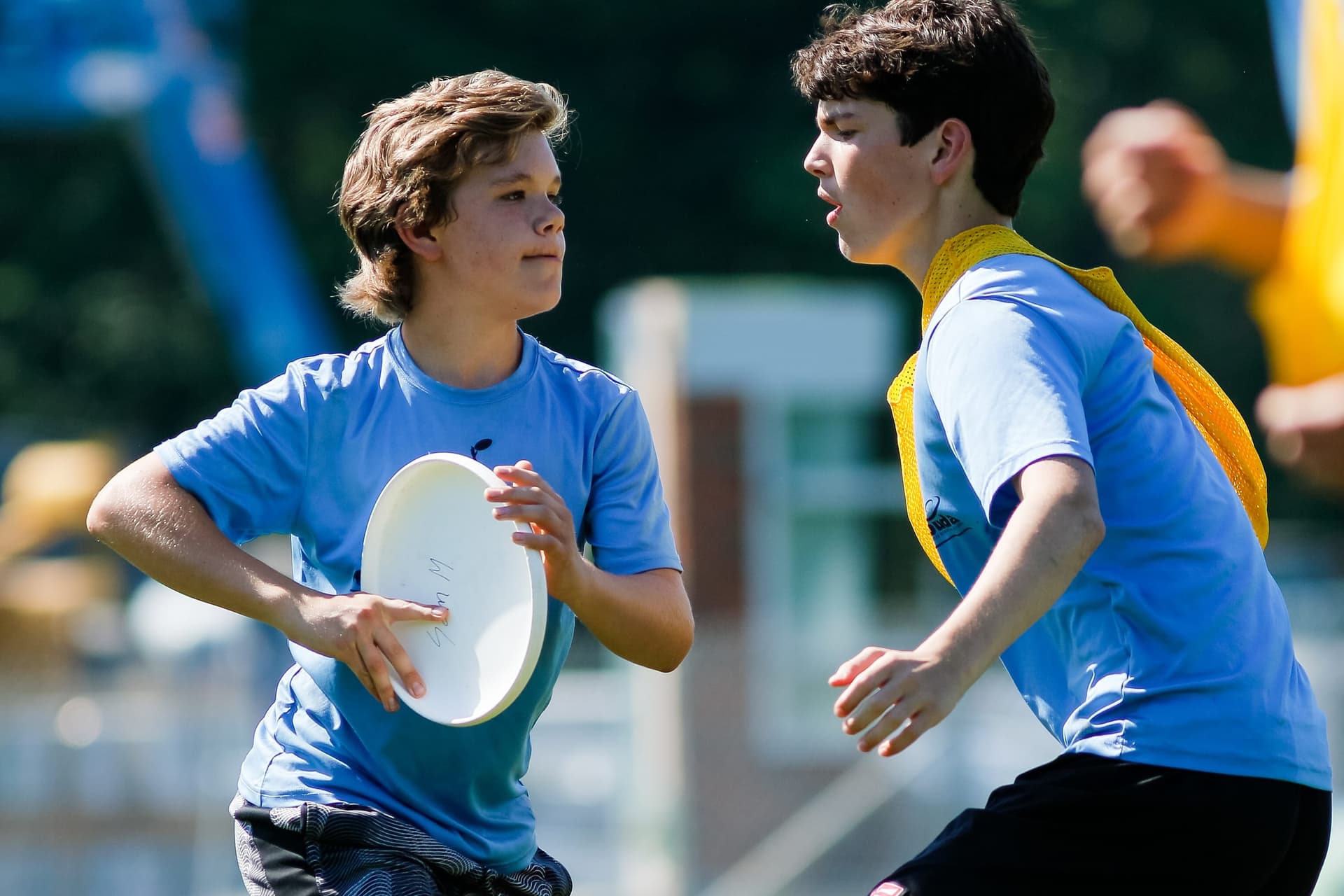 Middle-school player pivoting with the disc as a defender in a yellow pennie closes in